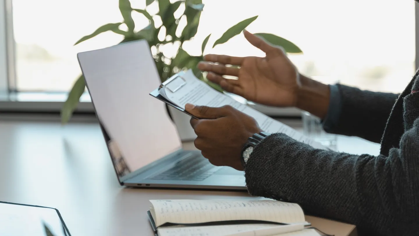 A person reviews business documents beside a laptop and notebook.