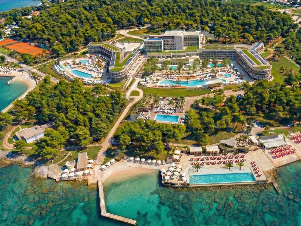Pogled iz zraka na resort Pical: hotelski kompleks s bazenima, teniskim terenima, borovom šumom i uređenim plažama uz more.